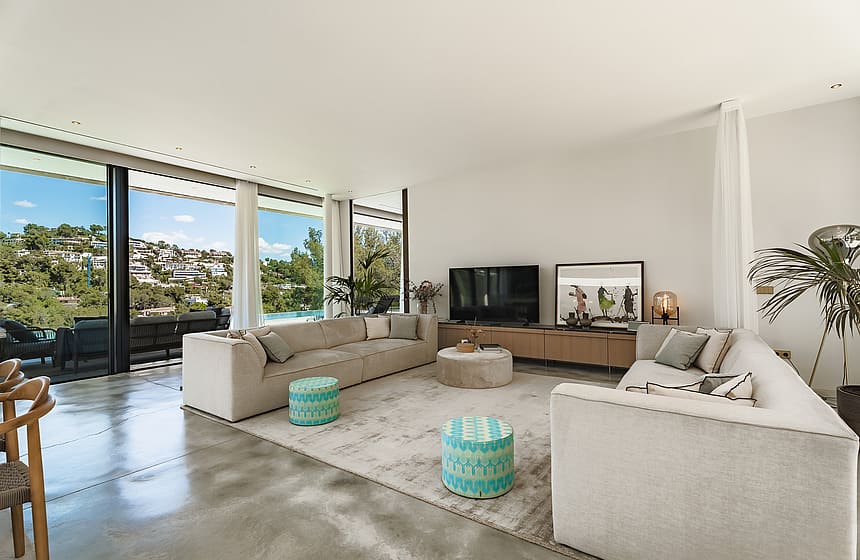 Modern living room with polished concrete floors, modular sofas, and full-height glass doors overlooking the hills.