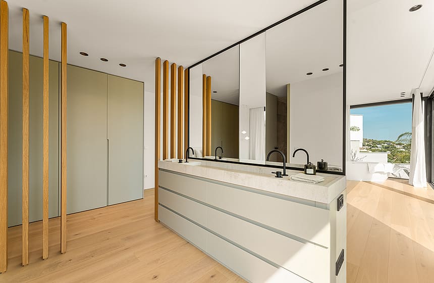 Modern master bathroom featuring a dual vanity with white stone countertop, black faucets, a large mirror, and light oak floors.