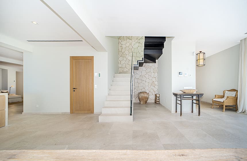 A wide entrance hall featuring a minimalist white stone staircase, a light oak wood door, and a textured stone feature wall.