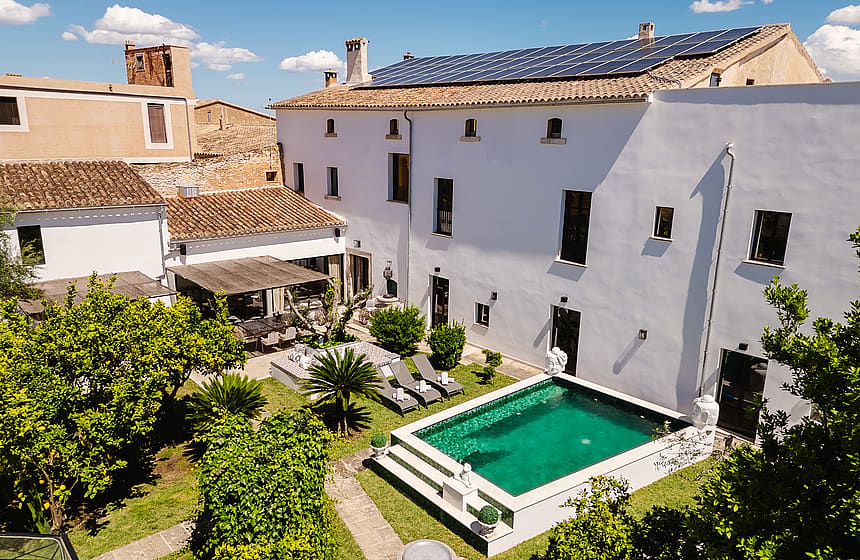 Aerial view of a white Mediterranean townhouse with a rectangular swimming pool, garden, and terracotta-tiled roof.