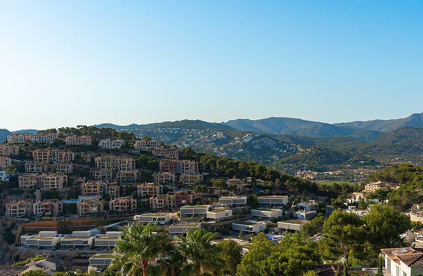 Aerial perspective of a hillside village in Port d'Andratx, showing terraced Mediterranean villas amidst dense vegetation.
