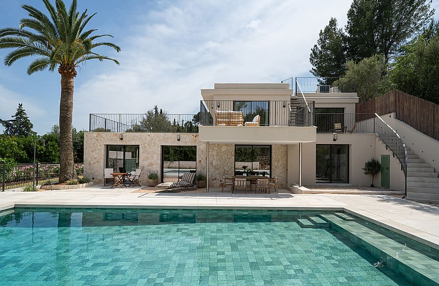 Facade of a two-story villa with pool in the foreground, exposed stone walls, and upper terrace.