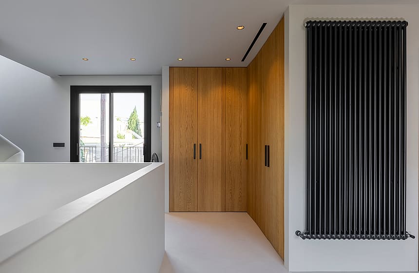 Modern hallway featuring custom oak wardrobes, a black vertical radiator, and natural light from a balcony door.