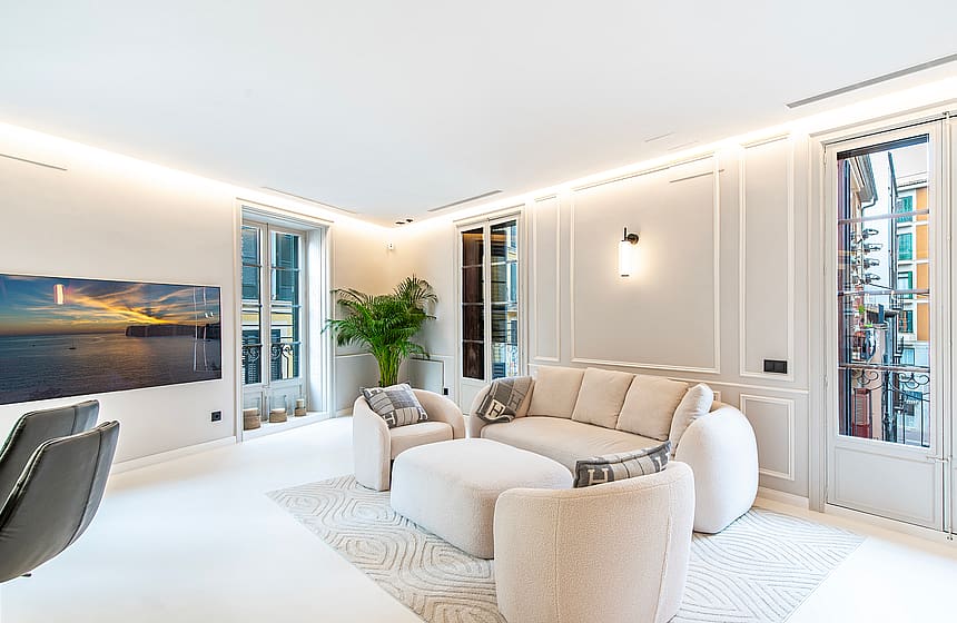A bright, modern living room featuring cream-colored textured armchairs, a large sofa, and white walls with vertical paneling.