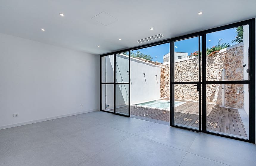 Modern interior living space featuring white walls, large black-framed glass sliding doors, and a view of a small pool.