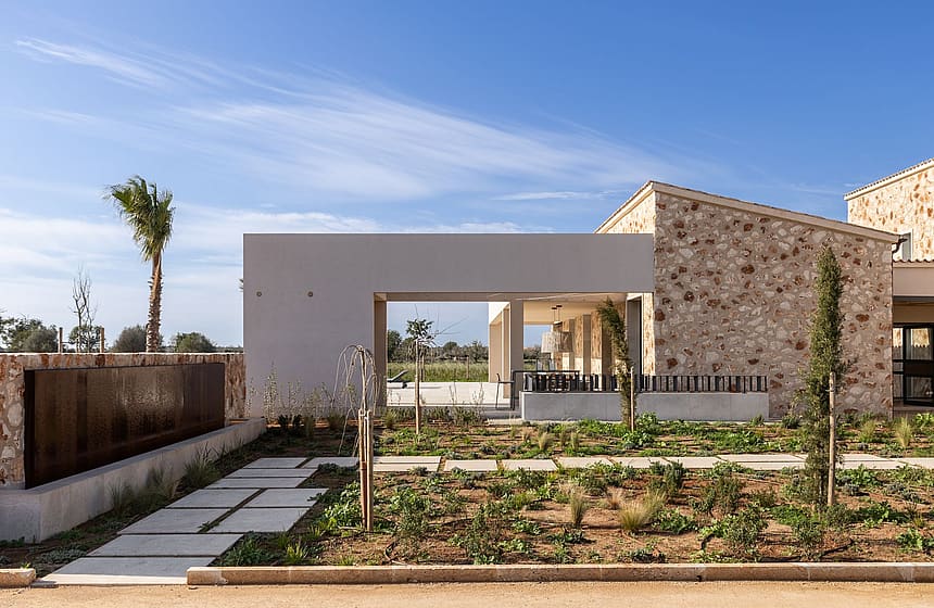Exterior view of a modern finca featuring traditional natural stone walls, a flat concrete overhang, and a landscaped garden.