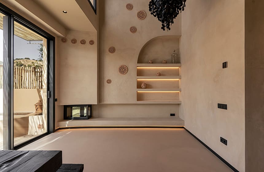 Empty living room with textured beige walls, built-in arched stone shelves, recessed lighting, and large sliding glass doors.