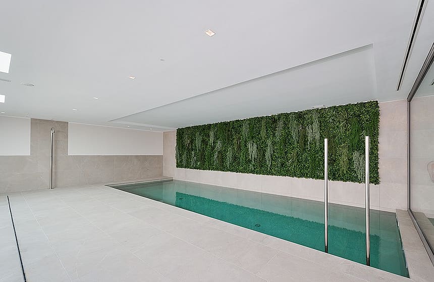 Piscina interior con agua turquesa, barandillas de acero y gran jardín vertical sobre suelo de piedra gris.