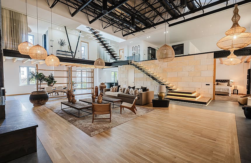 Double-height living space with light wood floors, a natural stone feature wall, and a dramatic steel staircase.