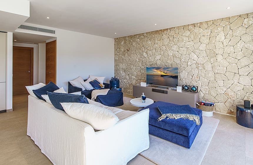 Modern living room featuring a textured natural stone wall, white sofa, blue armchairs, and neutral tiled flooring.
