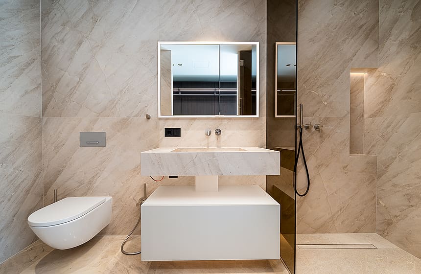 A modern bathroom featuring beige veined marble walls, a wall-hung white vanity, and a glass-enclosed walk-in shower.