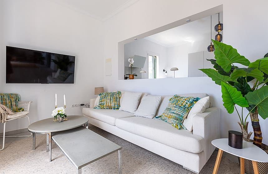 Living room featuring a light-colored sofa, a set of nesting coffee tables, wall-mounted television, and a large indoor plant.