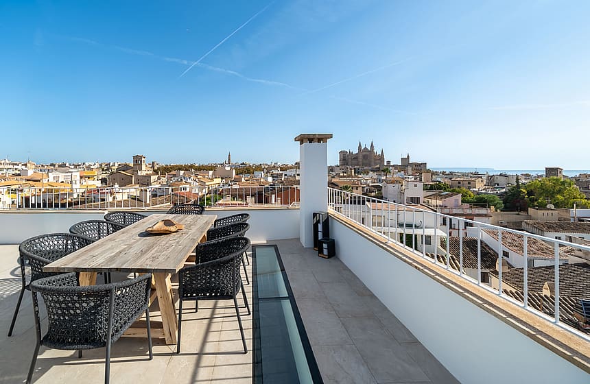 Expansive rooftop terrace with a wooden dining set overlooking the Palma city skyline and Cathedral under a clear blue sky.