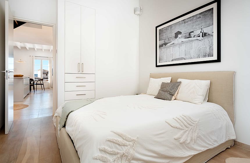 A minimalist bedroom featuring a beige upholstered bed, white textured bedding, and a framed black and white landscape print.
