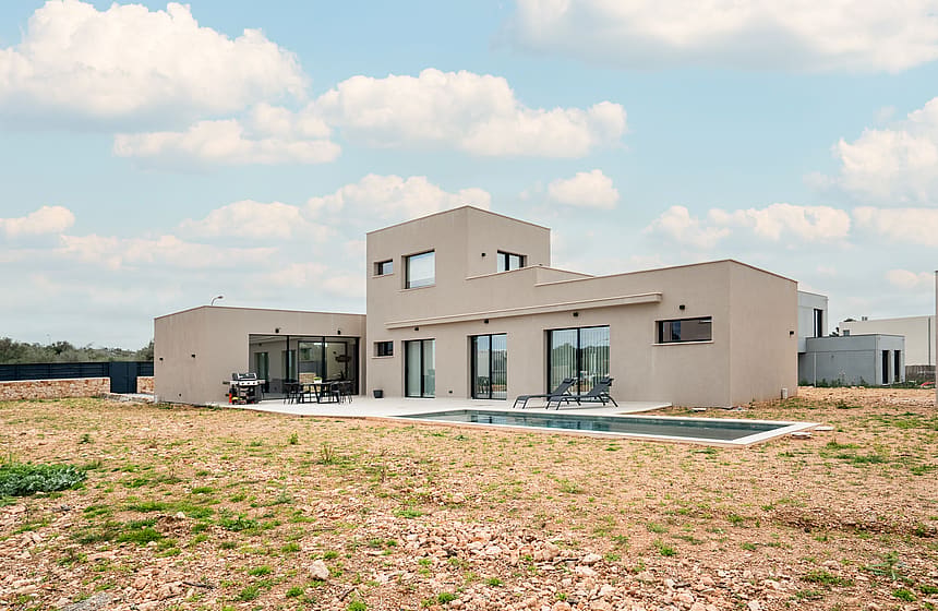Exterior view of a modern two-story beige villa with a swimming pool, flat roof, and large glass sliding doors.
