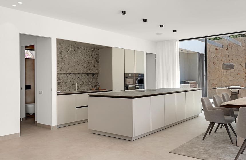 Handleless island kitchen with dark stone worktop, terrazzo-effect splashback and garden views