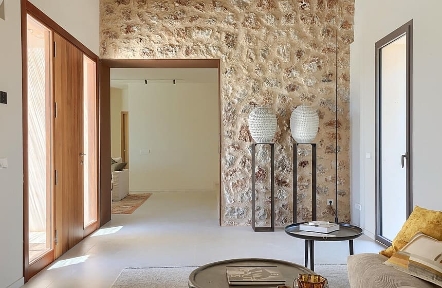 Interior view of an entrance hall featuring a tall dry stone wall, wooden doors, and two sculptural vases on metal stands.