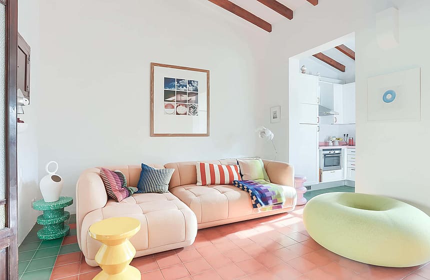 A living room interior featuring a beige modular sofa, terracotta floor tiles, exposed wooden ceiling beams, and a round lime green ottoman.
