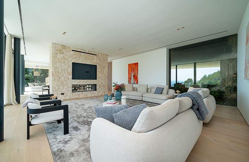 Spacious living room featuring a floor-to-ceiling natural stone wall with a fireplace, light wood flooring, and modern furniture.