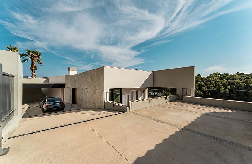 Wide view of a contemporary house exterior with a paved entrance, covered parking area, and light-toned masonry walls.