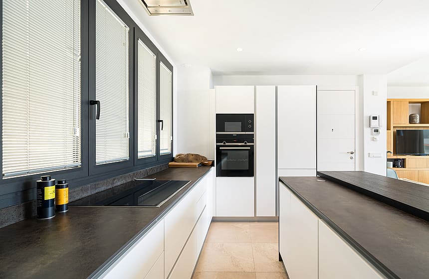 Modern kitchen featuring dark matte counters, white cabinetry, and large windows with integrated blinds.