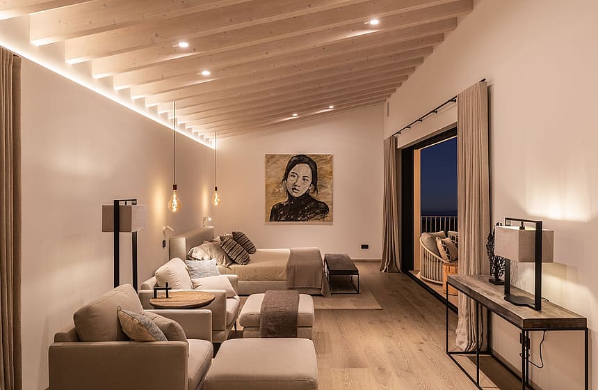 Spacious bedroom with a king-sized bed, seating area, and sliding glass doors opening to a terrace at dusk.
