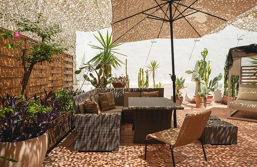 Outdoor terrace in Santa Catalina featuring woven lounge furniture, a large umbrella, and various potted cacti and plants.