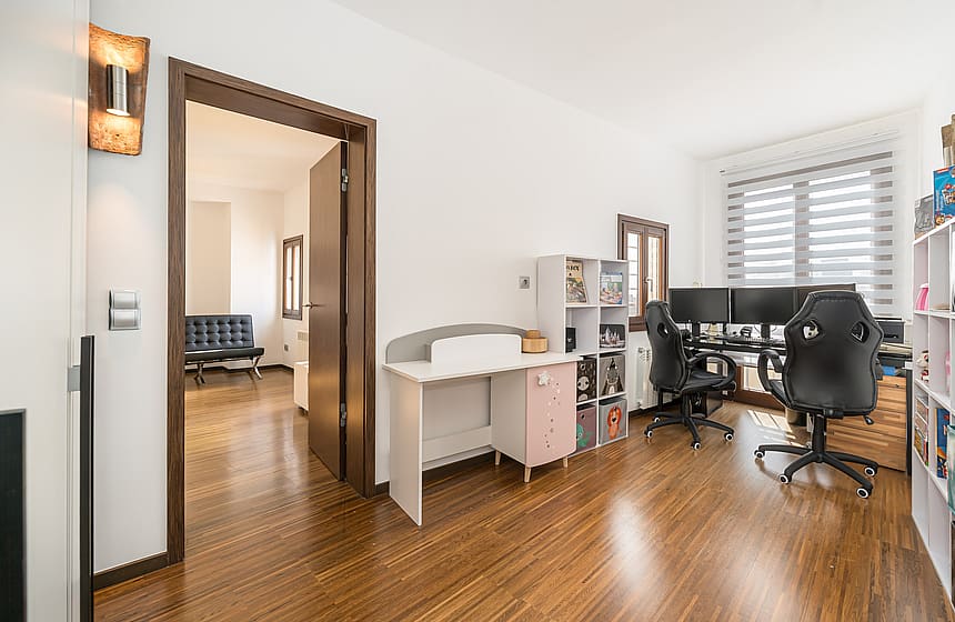 A bright room with dark wood floors, a desk with multiple monitors, and white storage shelving units.