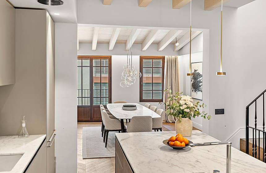 Kitchen island view to dining area featuring marble tables, exposed wood beams, grey chairs, and a wrought iron staircase.
