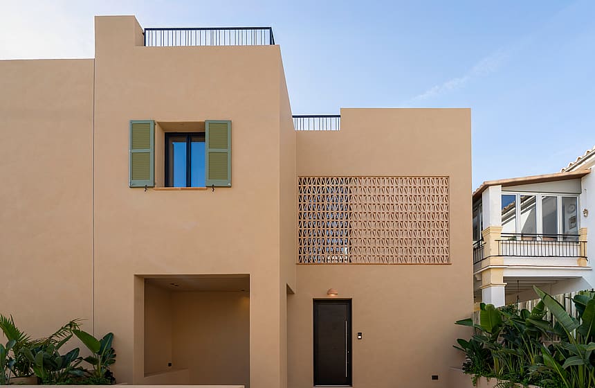 Two-story townhouse exterior with beige stucco walls, green window shutters, and a terracotta lattice screen by the entrance.