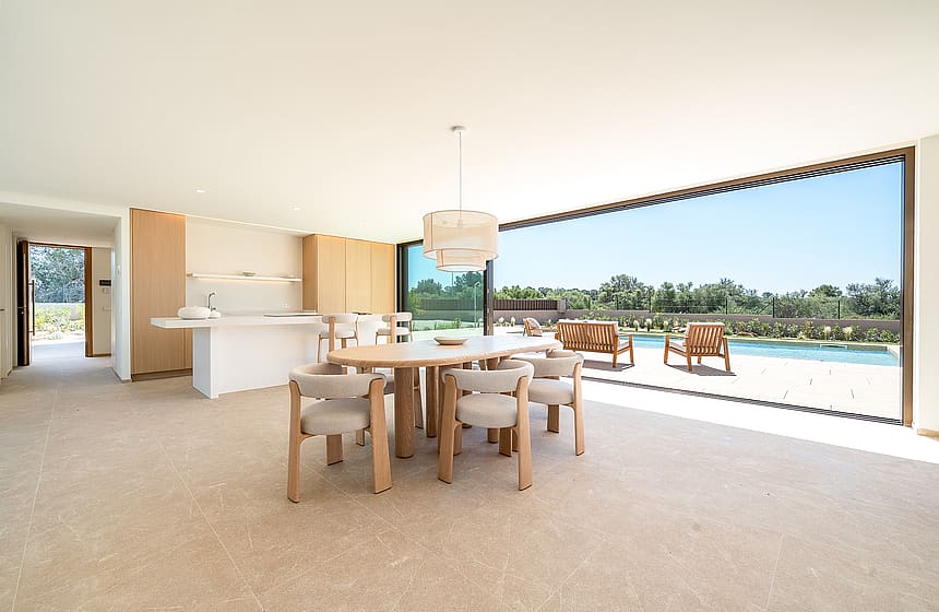 Bright dining area with oval wooden table and cream upholstered chairs, large sliding doors opening to an outdoor pool deck.