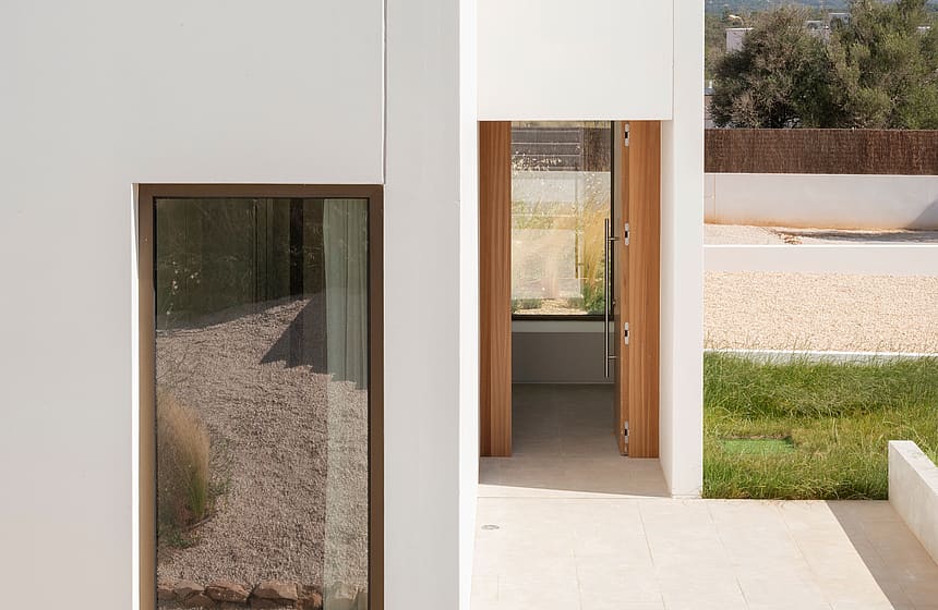A white modern building exterior featuring clean geometric lines, large windows, and a wooden entryway with mountain views.