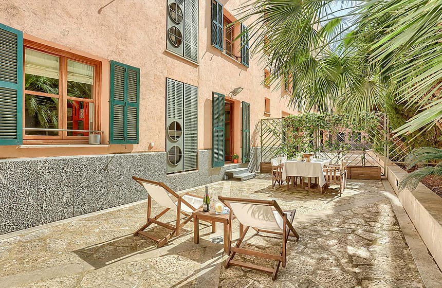 A private outdoor terrace in the Old Town featuring gravel flooring, white folding lounge chairs, a dining set, and pink stucco walls with green shutters.