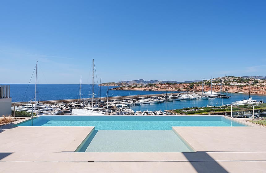A rectangular infinity pool with turquoise water in the foreground, framing a direct view of the marina and yachts.