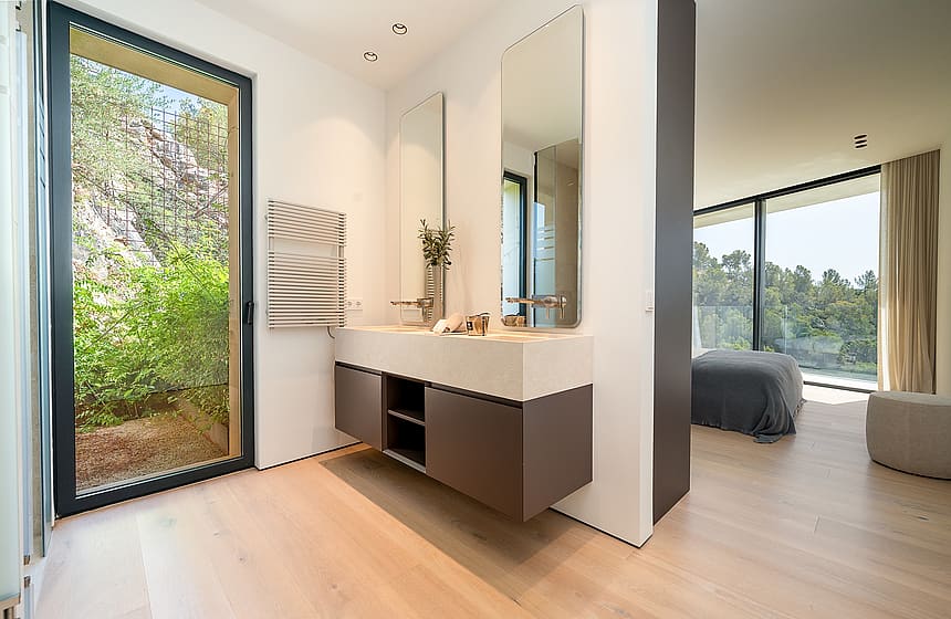 Modern master bathroom with a floating vanity, light oak flooring, and a glass door opening to a private garden area.