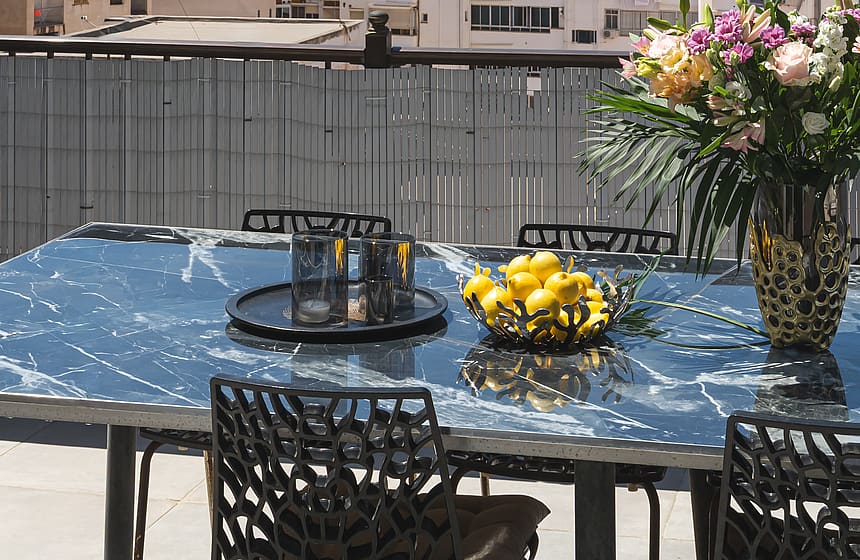 An outdoor terrace table set with a floral arrangement, overlooking a dense urban cityscape with mountains in the background.