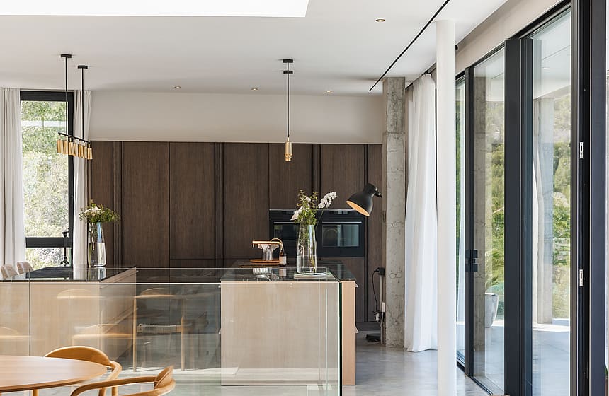 Modern kitchen featuring a central island, dark wood wall units, and floor-to-ceiling windows in a bright interior.