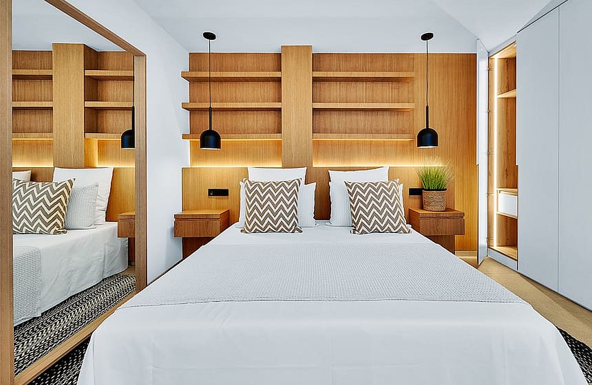 A modern bedroom featuring a bed with patterned throw pillows, oak-finished shelving, and integrated lighting.