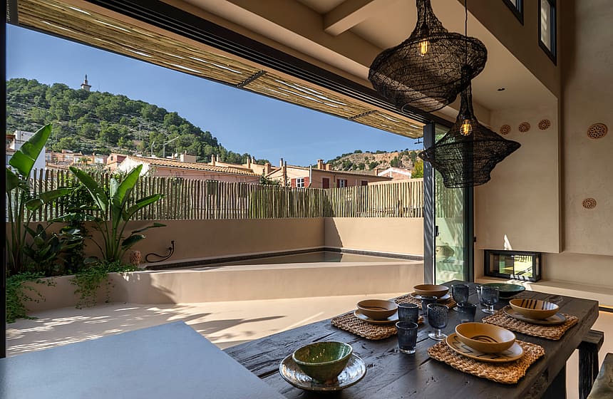 Dining room with large sliding doors opening to an outdoor terrace with a pool, overlooking a hillside.