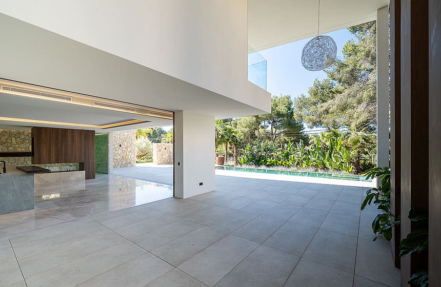 Interior view of a contemporary living area with large floor-to-ceiling glass doors opening onto a sunlit pool terrace.