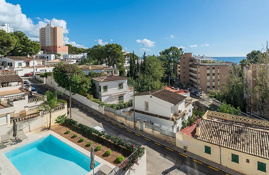 High-angle view of a rectangular outdoor swimming pool with blue water and surrounding residential buildings in a coastal area.