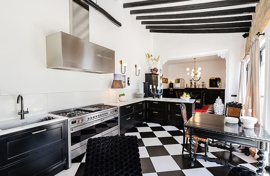 Kitchen features black and white checkered tile floors, black cabinets, a stainless steel range, and exposed dark wood beams.