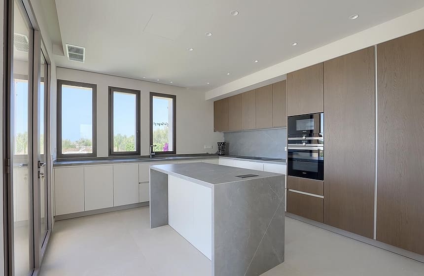 Modern kitchen featuring a grey stone island, wood-veneer cabinetry, and white countertops against a neutral wall backdrop.