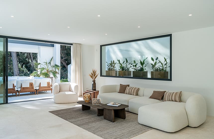 Spacious open-plan living room with bouclé sofas, stone flooring and floor-to-ceiling sliding doors opening to the pool terrace