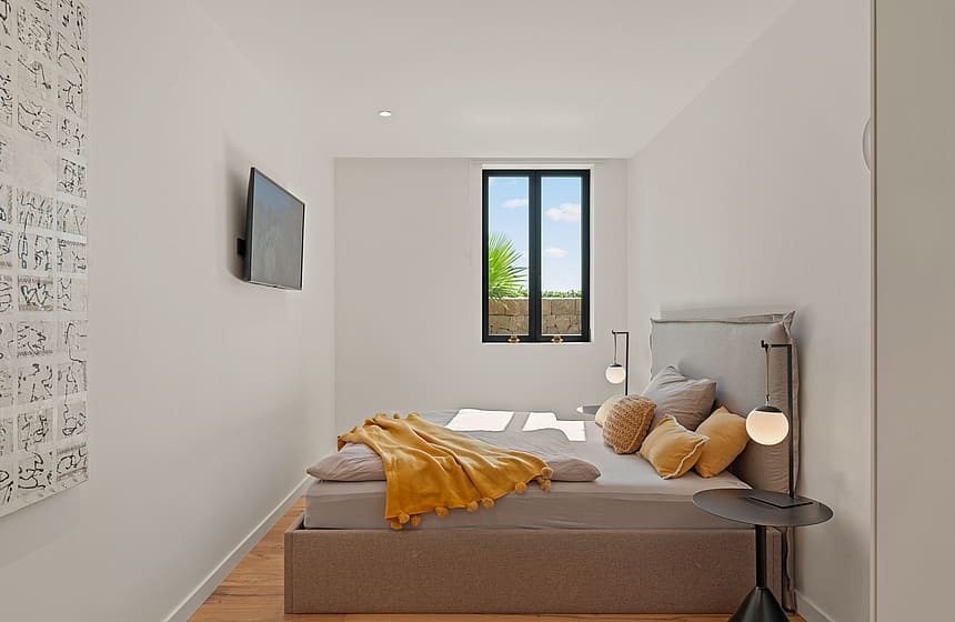 A modern bedroom featuring a bed with a grey upholstered headboard, a golden-yellow throw blanket, and a minimalist side table.
