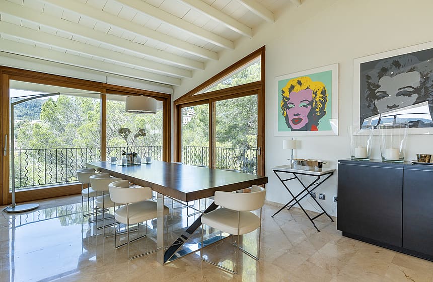 Large open-plan reception room with white beam ceilings, marble floors and art-hung wall leading to dining area