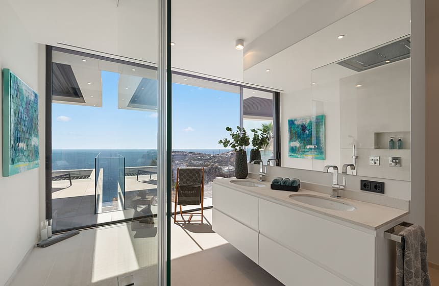 Modern bathroom featuring a double vanity, large mirror, and expansive window overlooking the sea.