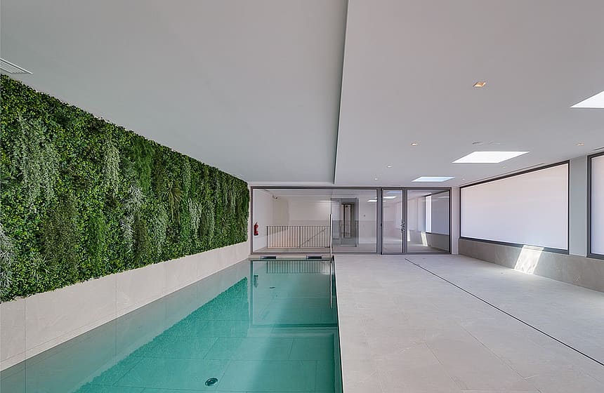 Rectangular indoor lap pool with full-length living plant wall to one side, skylights above and floor-to-ceiling glazing at the far end