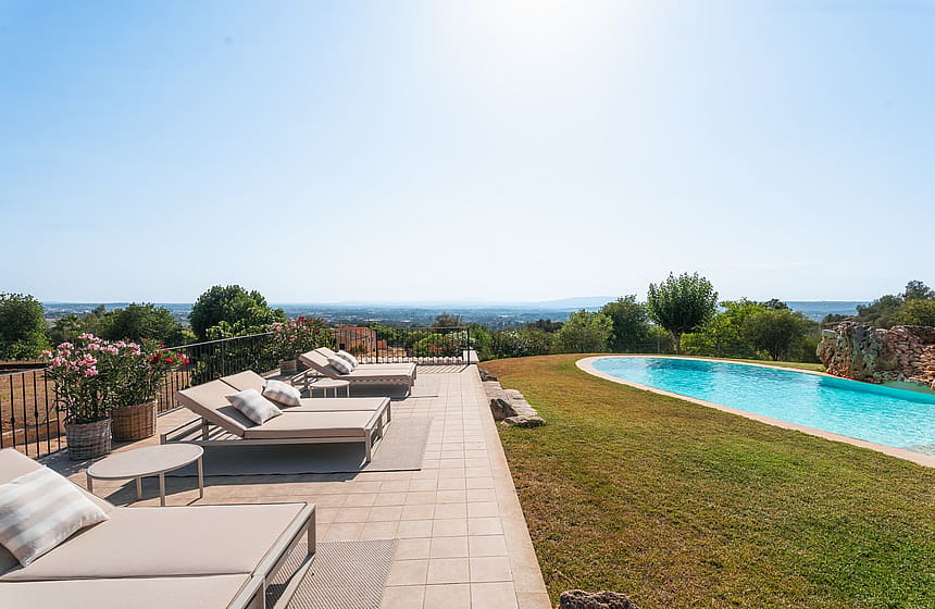Terraza de piscina en Manacor con tumbonas sobre pavimento hacia el paisaje montañoso lejano.