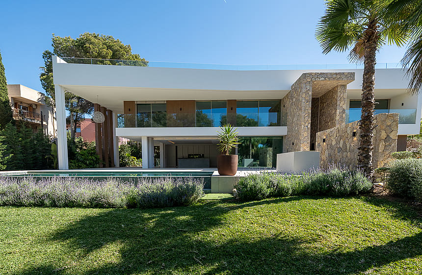 Exterior view of a two-story modern villa in Santa Ponsa featuring white plaster, natural stone walls, and a swimming pool.